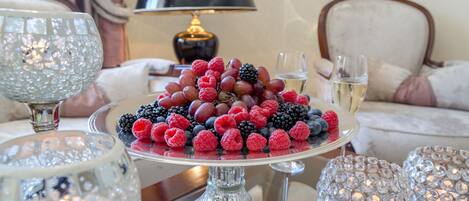 A dining table with a fruit platter, crystal glasses, and a lamp in the background.