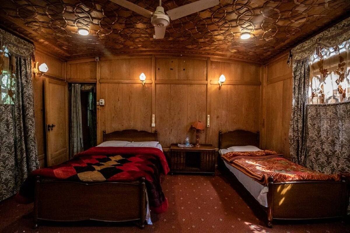 A room with two wooden beds, a ceiling fan, and wall-mounted lamps.
