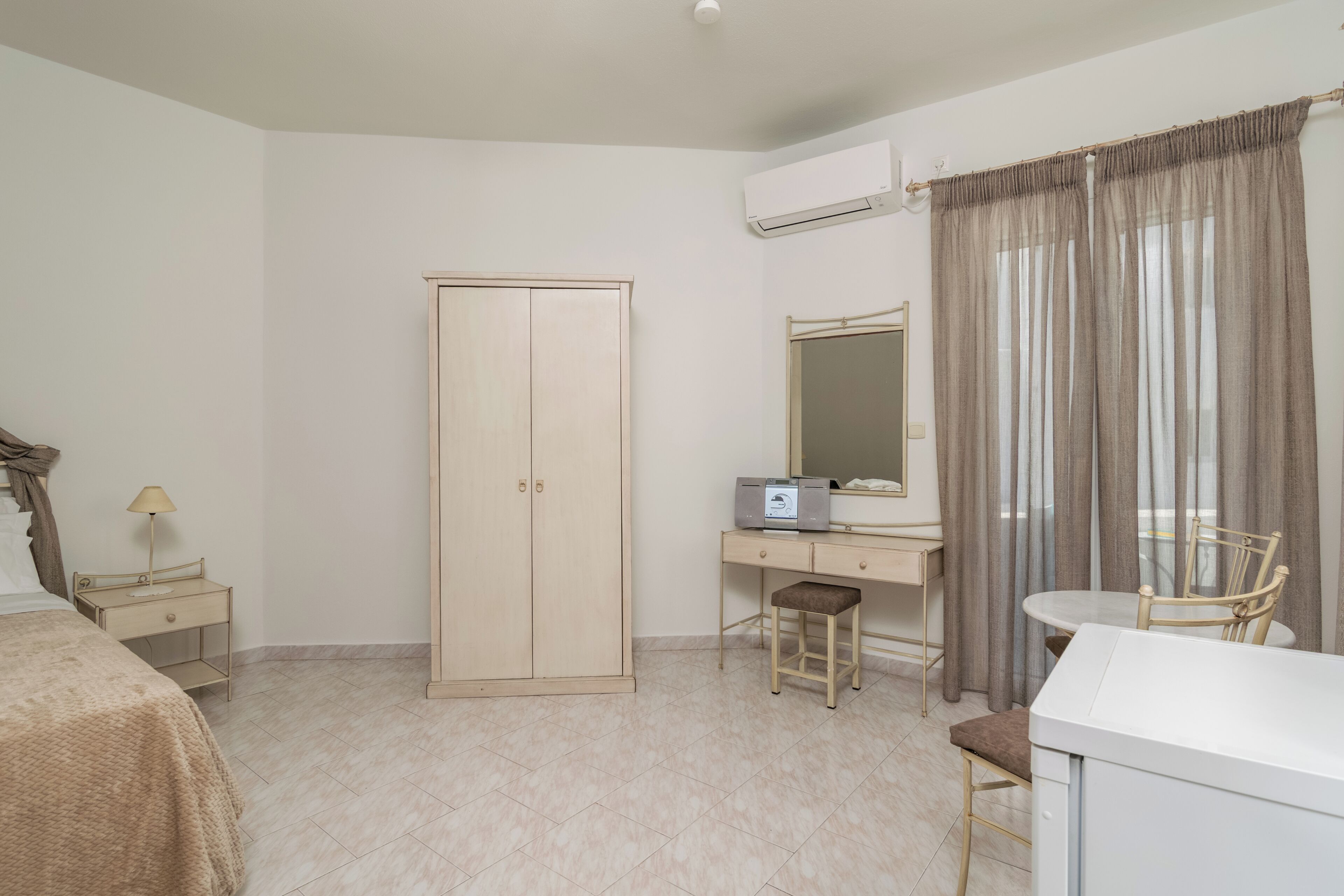 A bedroom with a bed, a wardrobe, a desk with a chair, a small stool, and a mirror.