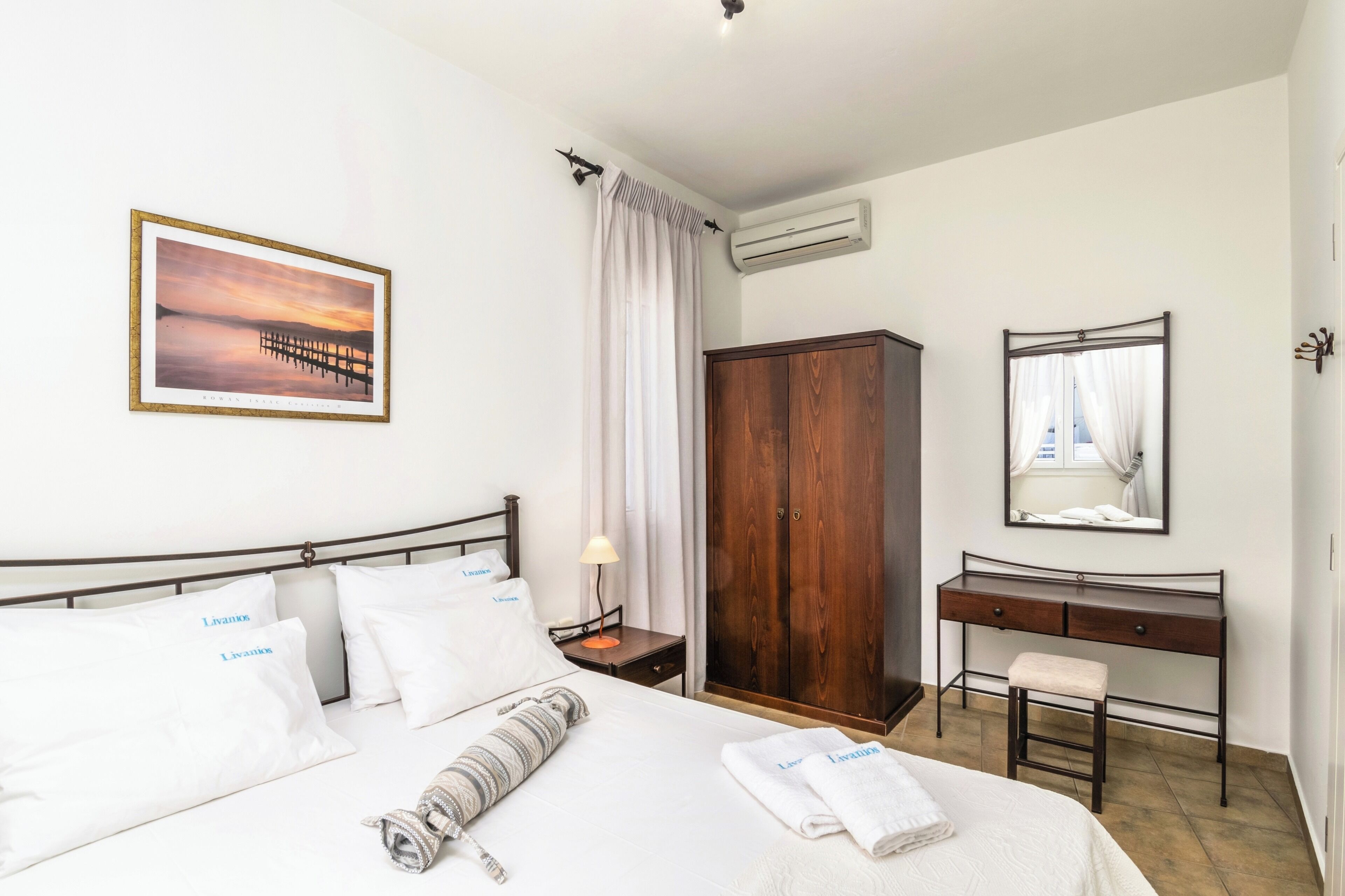 Una habitación de hotel con una cama, un armario de madera, un escritorio, un espejo y un cuadro en la pared.