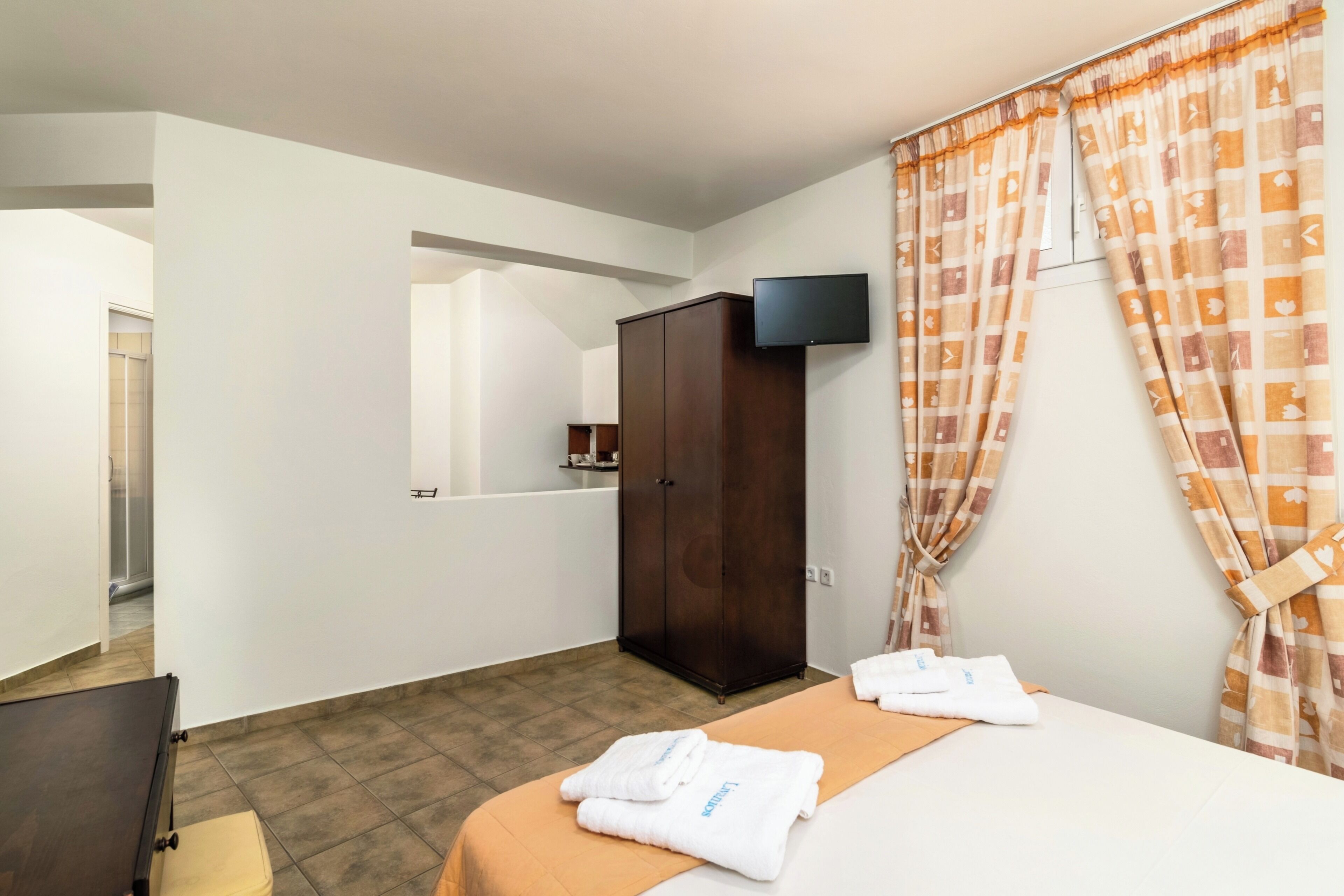 A hotel room with a bed, a wardrobe, a television, and a bathroom visible through an open door.