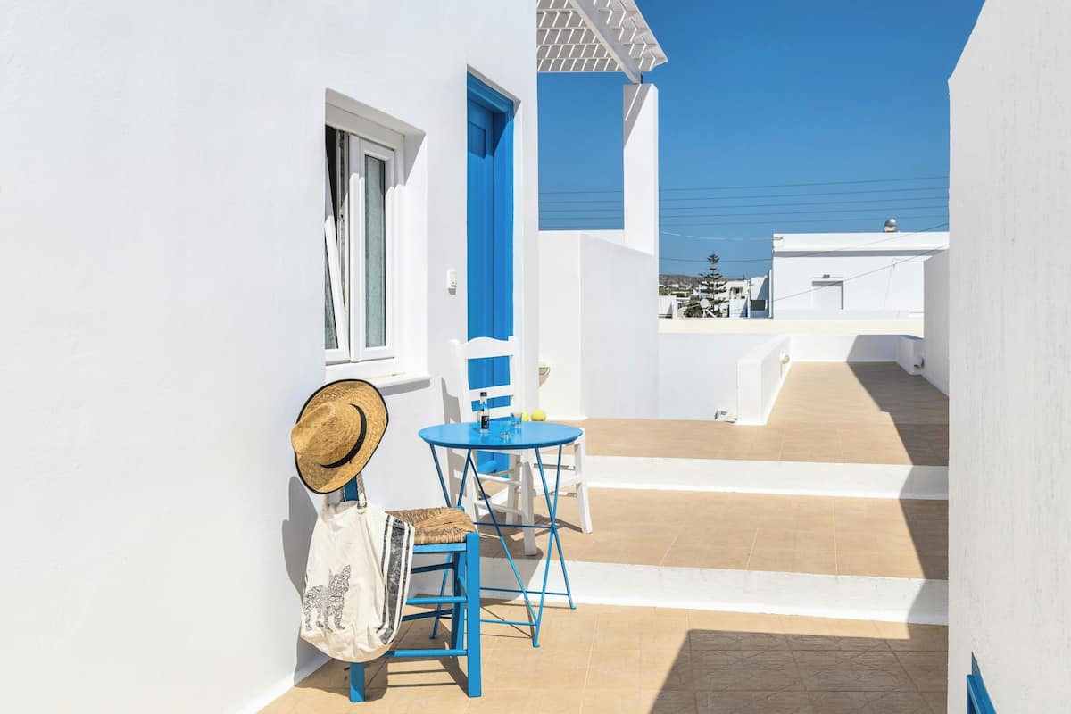 A white building with blue accents, a small table with chairs, a hat, and a bag.