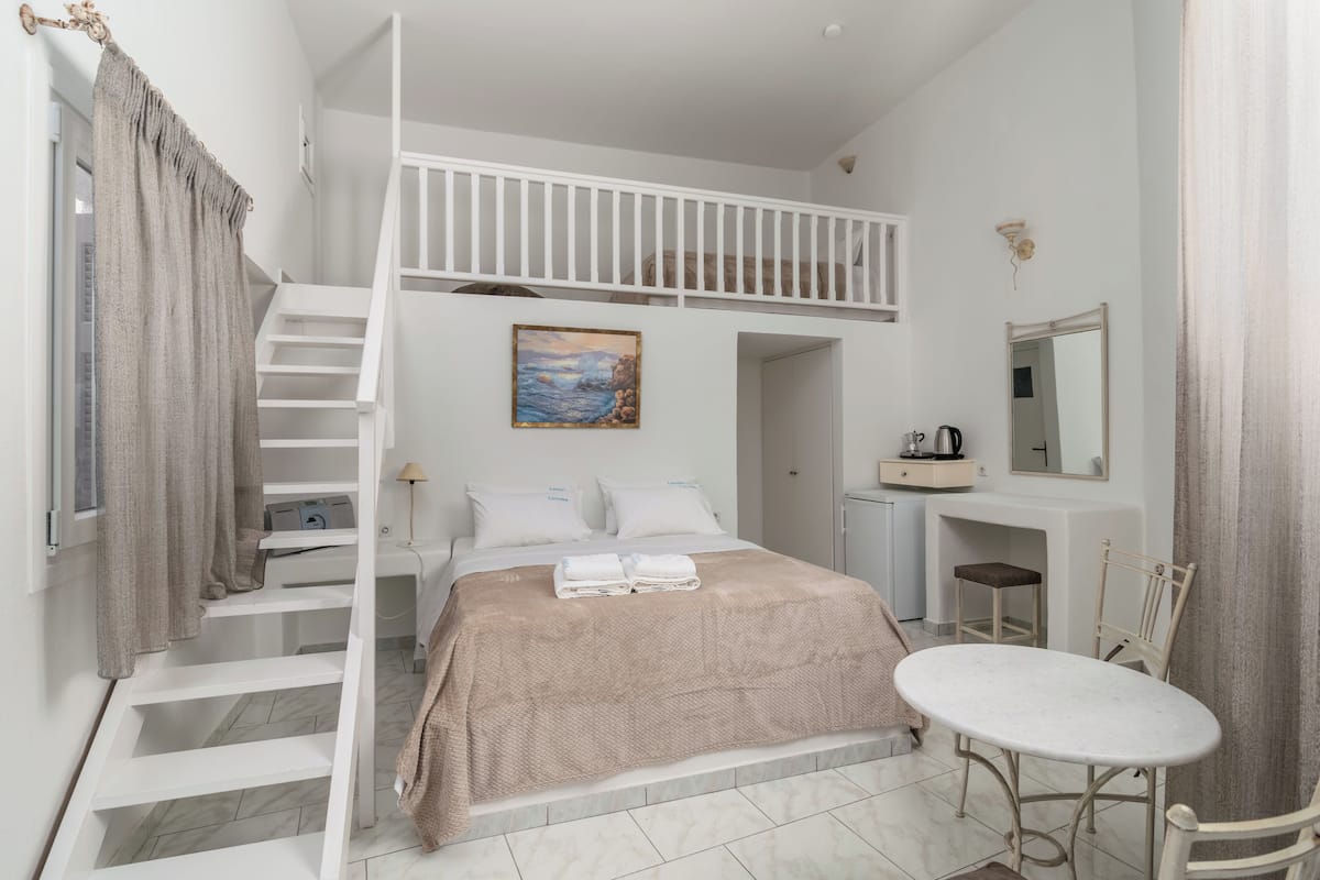 A bedroom with a bunk bed, a desk, a chair, a small table, a painting, and a mirror.