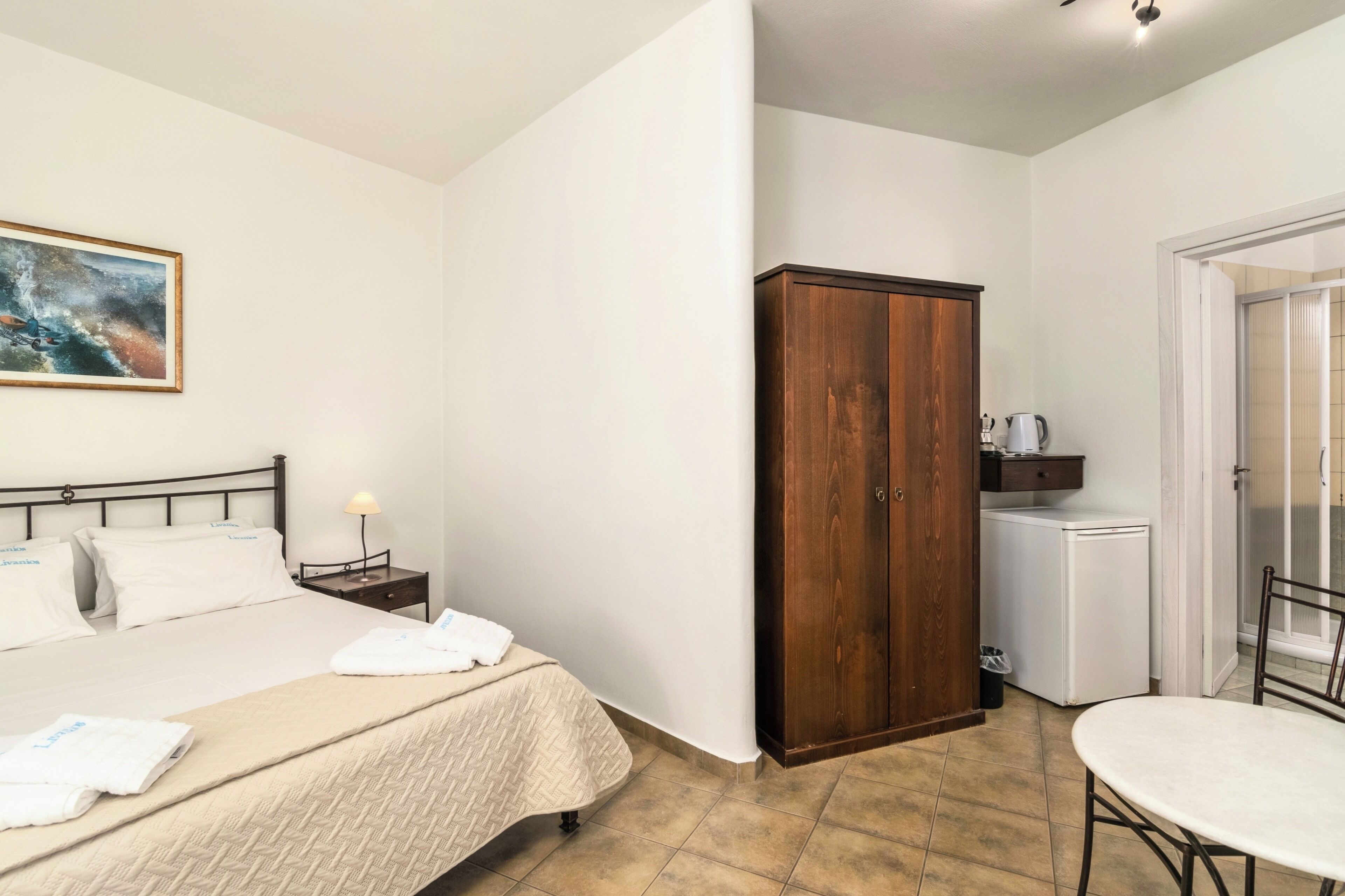 A hotel room with a bed, a wooden wardrobe, a small kitchenette, and a dining table.