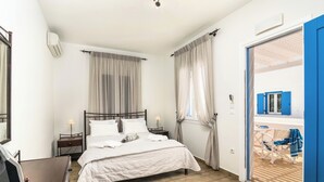 A bedroom with a bed, bedside tables, a chair, and a view of an outdoor area with a chair and table. - Livanios Studios (Milos)