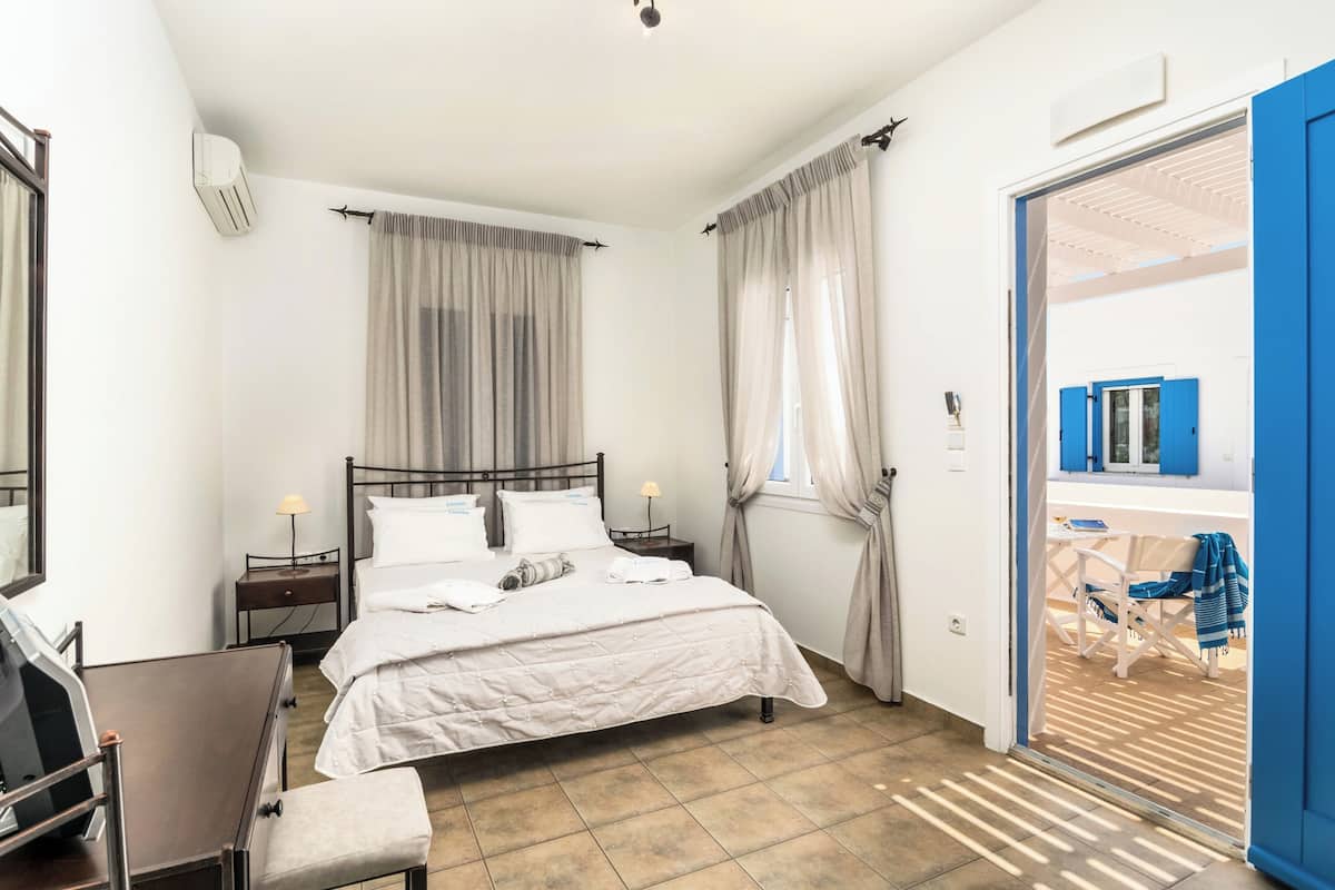A bedroom with a bed, bedside tables, a chair, and a view of an outdoor area with a chair and table.