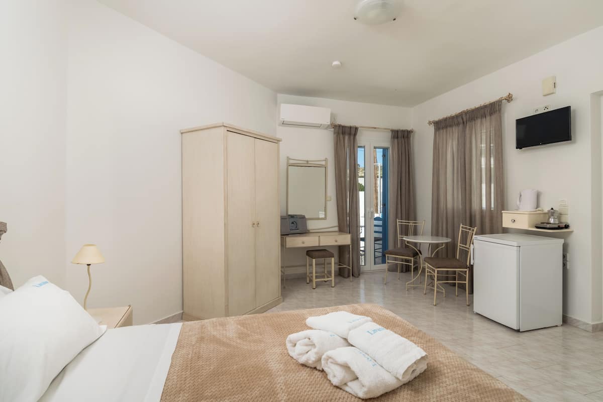 A hotel room with a bed, a desk, a chair, a small refrigerator, a television, and an air conditioning unit.