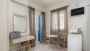 A room with a desk, chair, small table, and a refrigerator. - Livanios Studios (Milos)