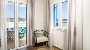 A balcony with a chair and table, a view of buildings, and a door with curtains. - Livanios Studios (Milos)