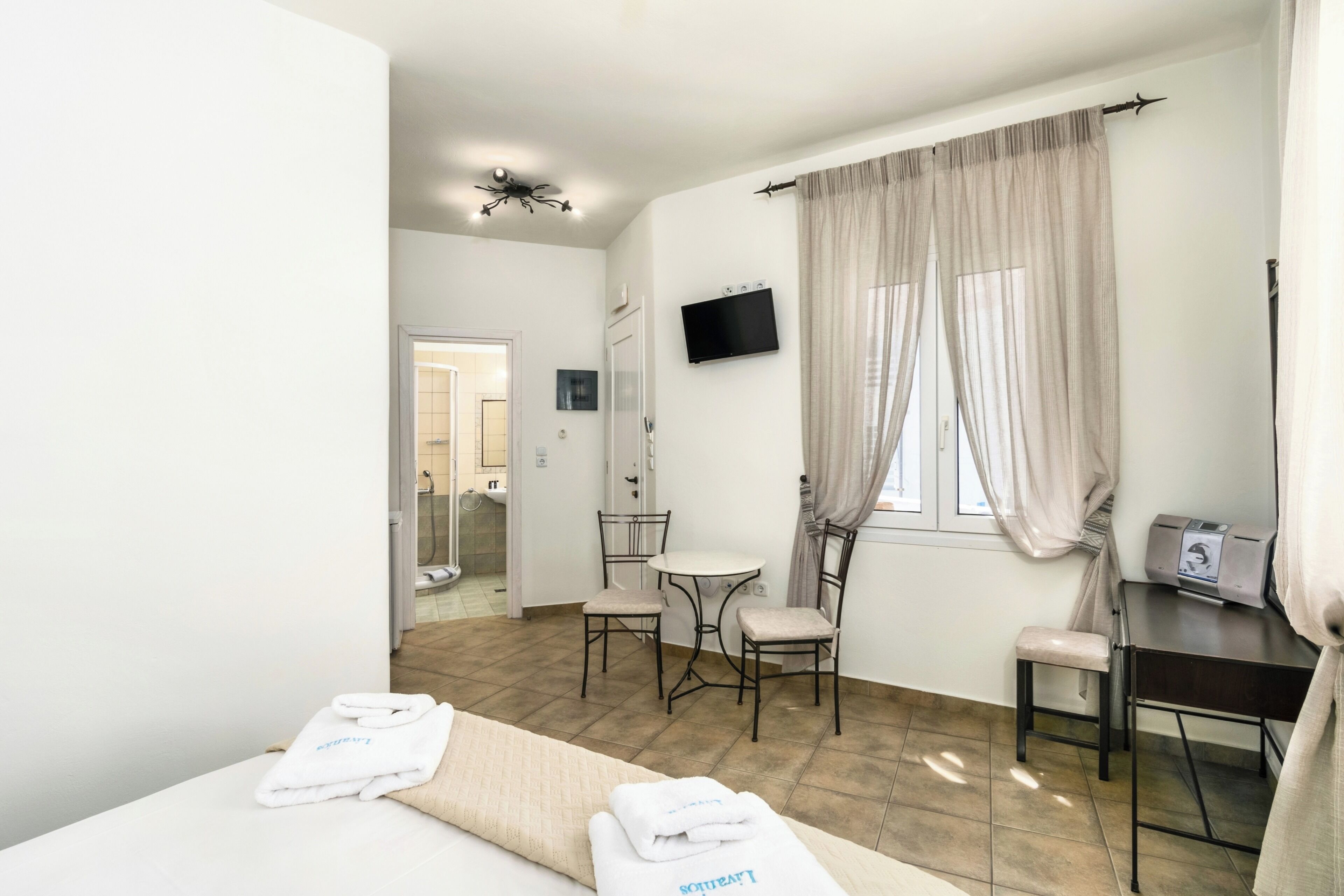 Habitación de hotel con cama, escritorio, silla, televisor y ventana con cortinas.