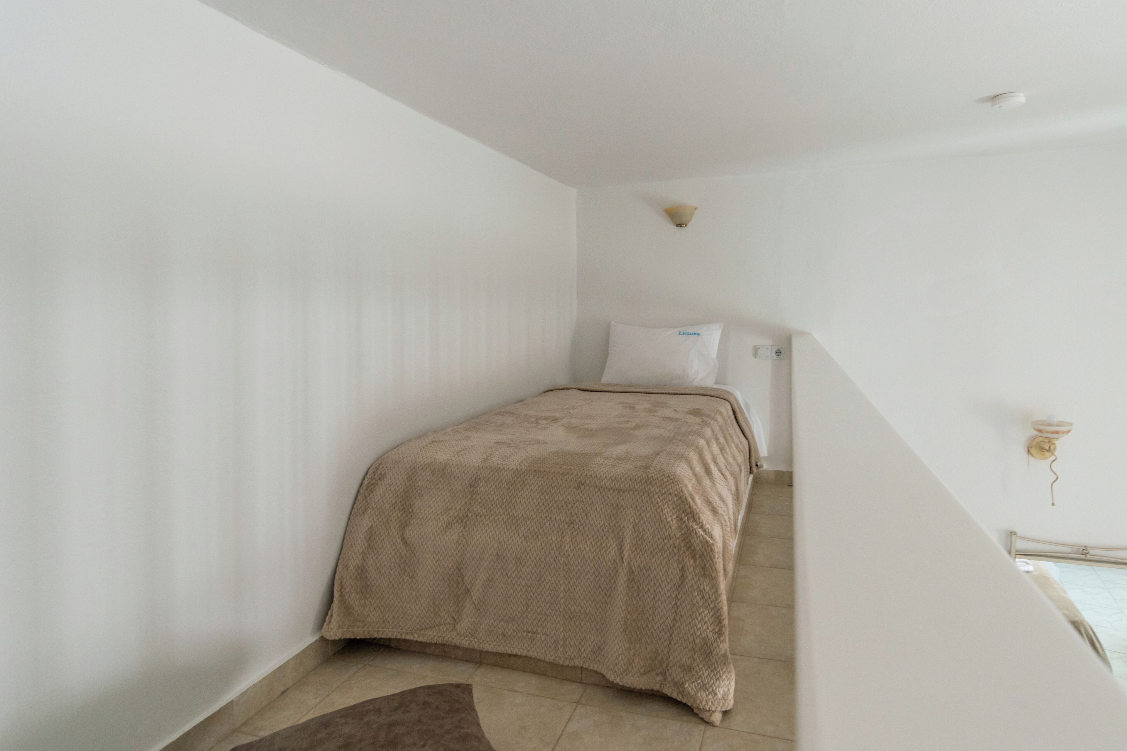 A bedroom with a bed, a pillow, a wall-mounted light fixture, and a staircase.