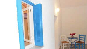 A room with a white wall, a blue door, a small table with chairs, and a stone floor. - Livanios Studios (Milos)