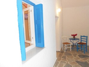 A room with a white wall, a blue door, a small table with chairs, and a stone floor. - Livanios Studios (Milos)
