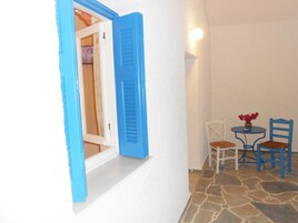 A room with a white wall, a blue door, a small table with chairs, and a stone floor.