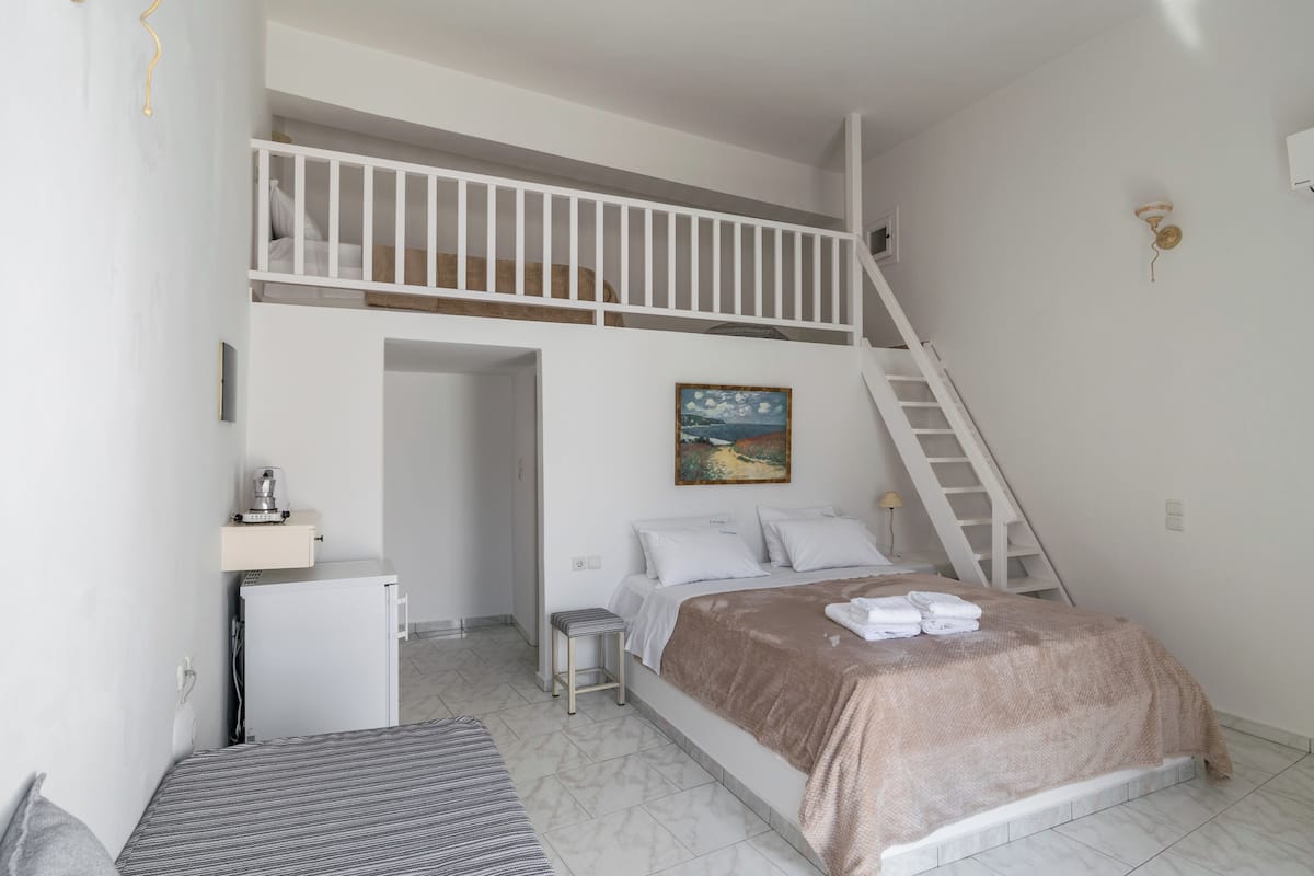 A bedroom with a bunk bed, a desk, a chair, a small refrigerator, and a painting on the wall.