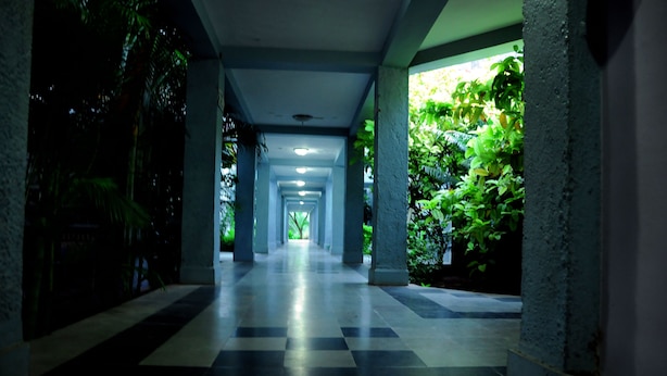 A corridor with a checkered floor, columns, and greenery on the sides. - KSTDC Hotel Mayura Bhuvaneshwari (Hospet)