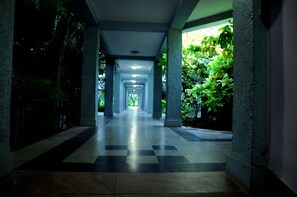 A corridor with a checkered floor, columns, and greenery on the sides.