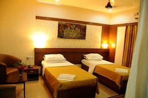 A hotel room with two beds, a wooden headboard, a nightstand with a lamp, and a wall-mounted artwork.