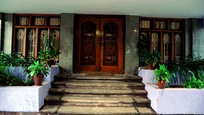 A set of stone steps leading to a wooden double door with intricate carvings, flanked by two rows of potted plants. - KSTDC Hotel Mayura Bhuvaneshwari (Hospet)