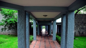 A covered corridor with a tiled floor, blue columns, and a stone wall on one side. - KSTDC Hotel Mayura Bhuvaneshwari (Hospet)