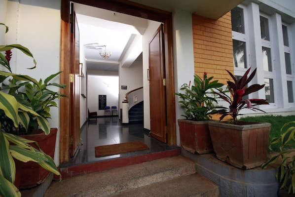 Entrada de un hotel con puerta de madera, una escalera y plantas en macetas.