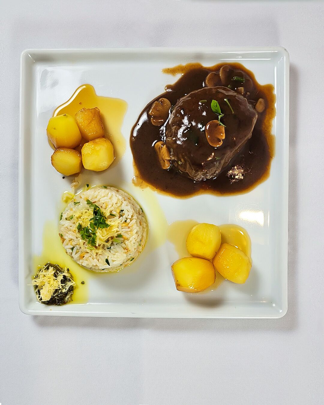 Un plato cuadrado con un guiso de carne, patatas y arroz.