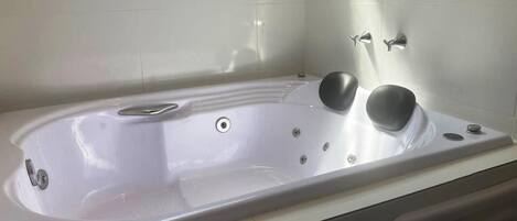 A white bathtub with a built-in seat and controls, a showerhead, and a drain.