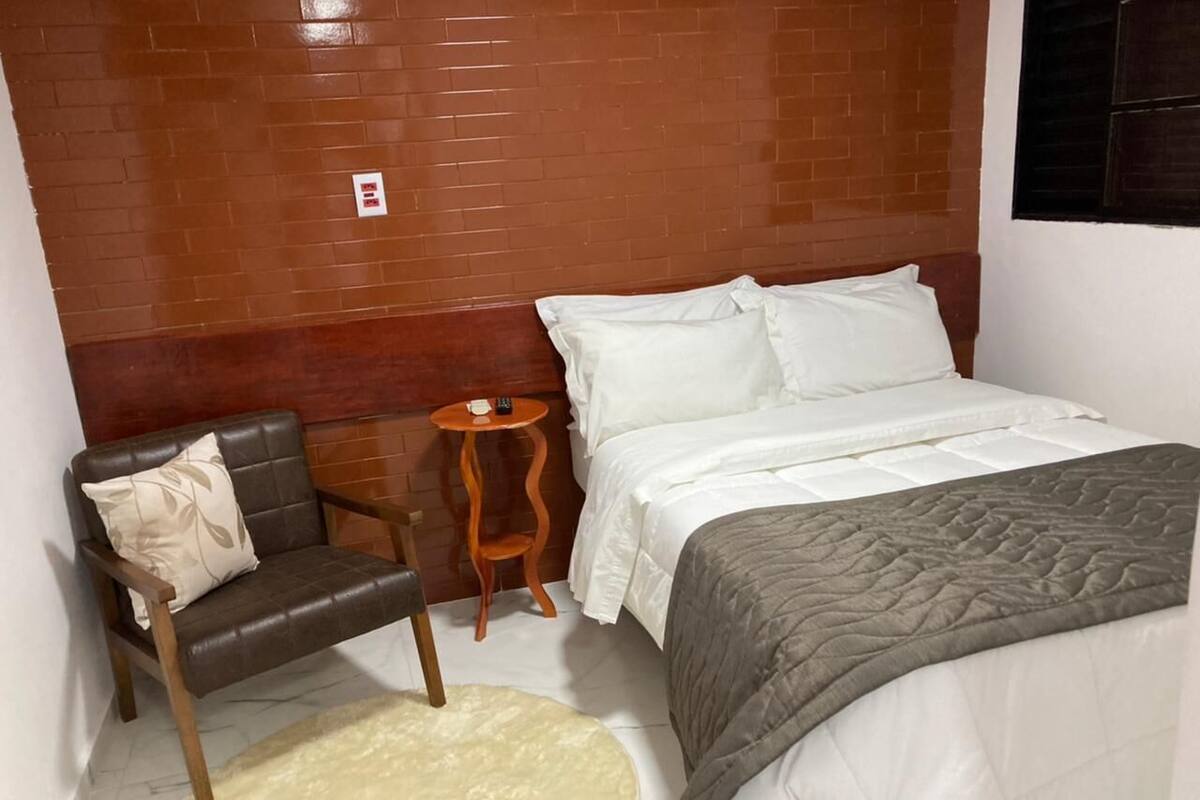 Ein Schlafzimmer mit Bett, Sessel, kleinem Tisch und Teppich.