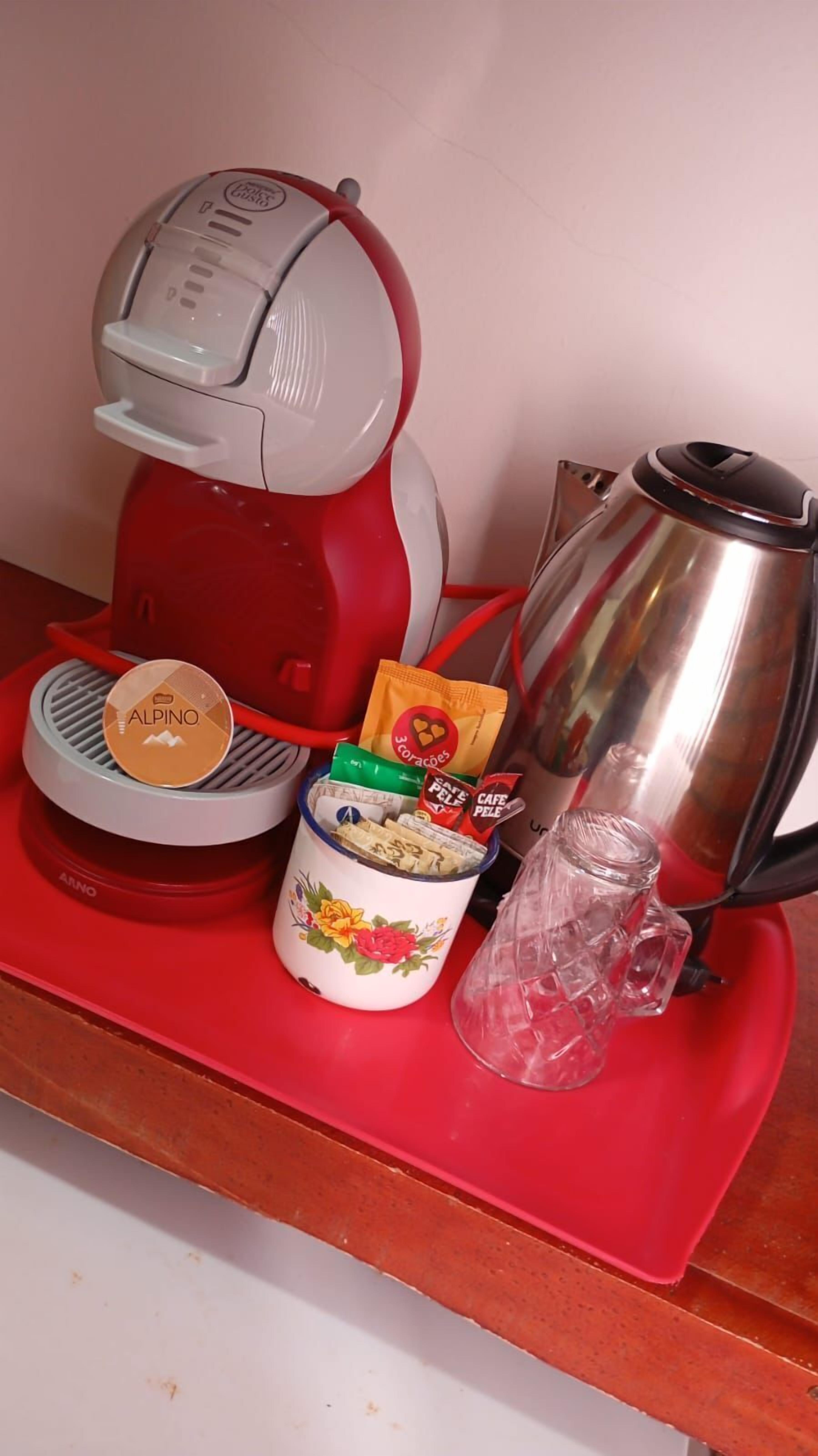 A red kitchen counter with a coffee maker, a kettle, a jar of coffee, and a small glass pitcher.