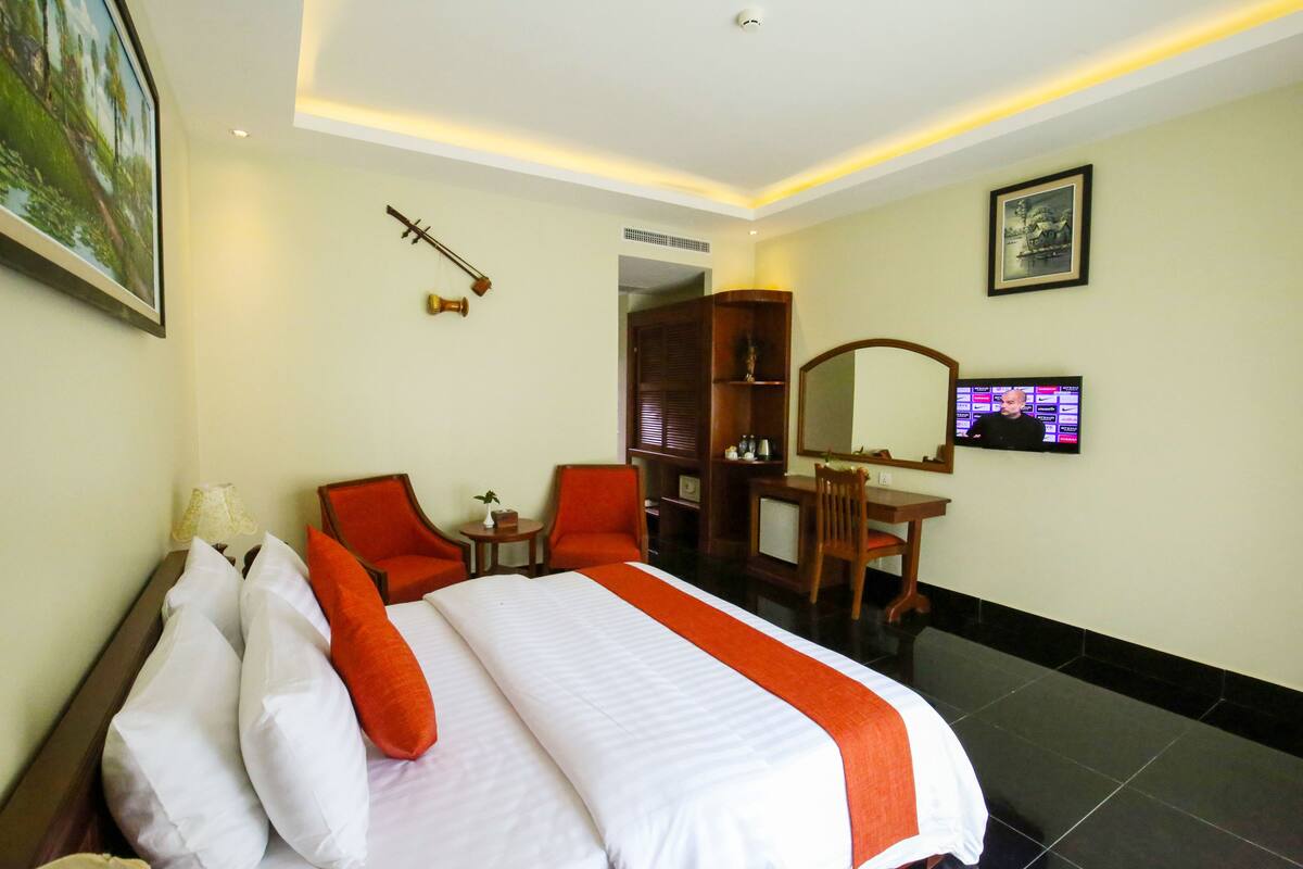 A hotel room with a bed, two chairs, a desk, a television, and a mirror.