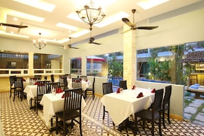 Ein Restaurant mit mehreren Tischen und Stühlen, Deckenventilatoren und großen Fenstern mit Blick ins Freie.