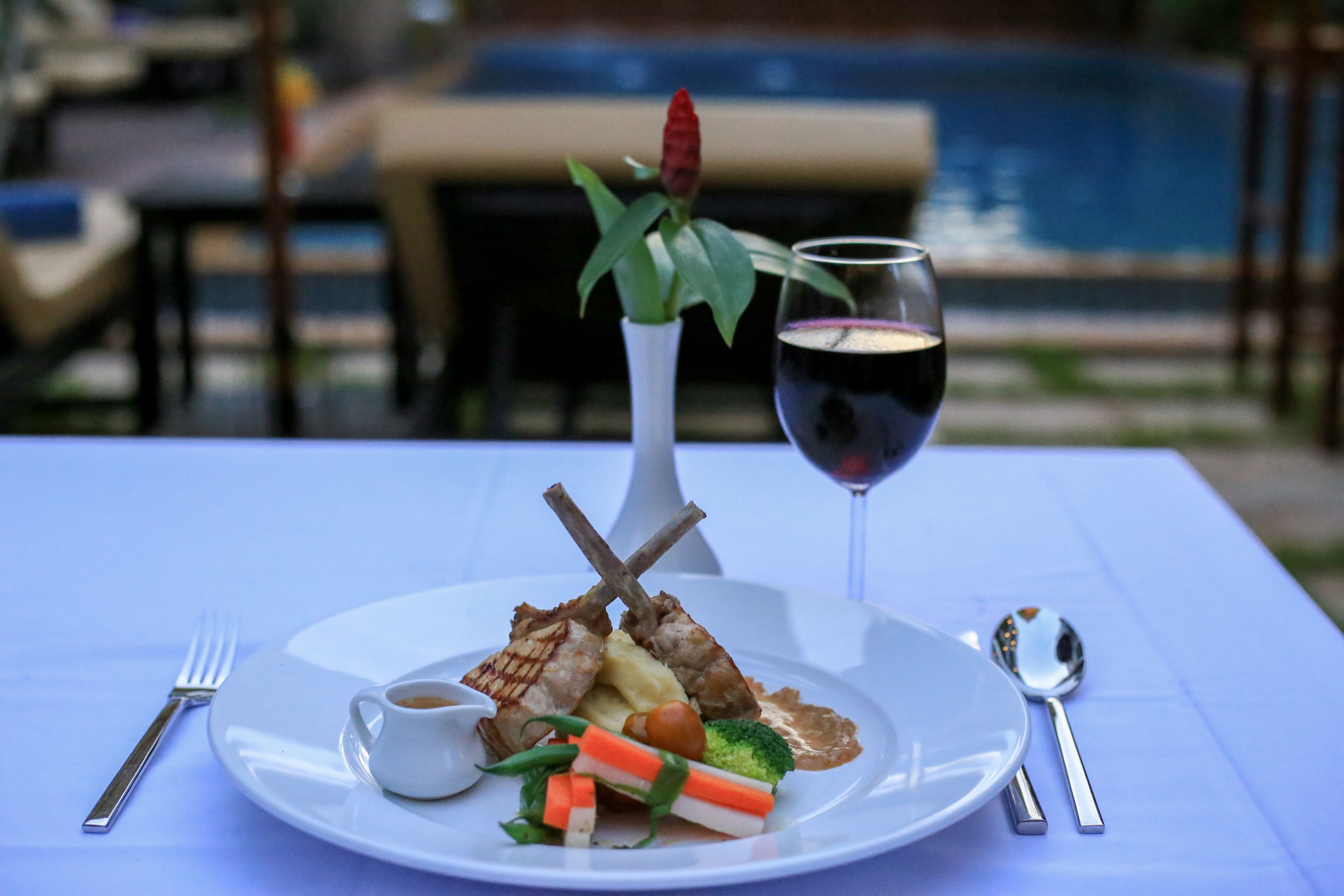 A dining table with a plate of food, a glass of red wine, and a small vase with a plant.