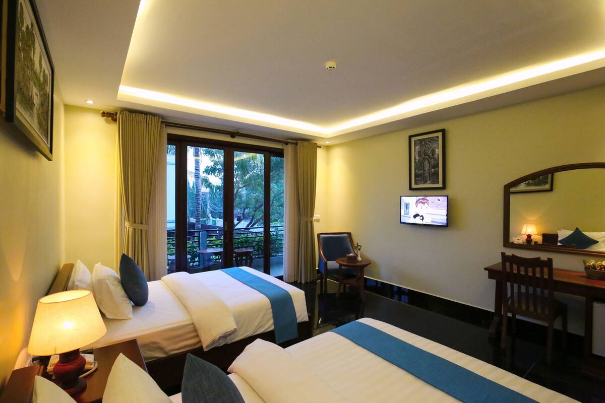 A hotel room with two beds, a desk, a chair, a TV, and a balcony with curtains.