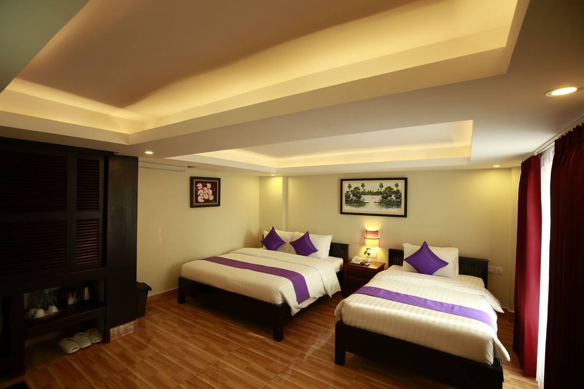 A hotel room with two beds, wooden flooring, a dark wooden cabinet, and a small shelf with shoes.