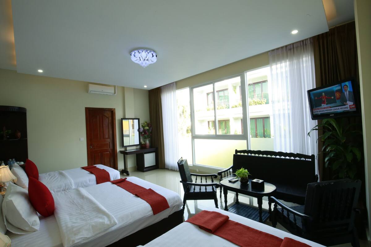 A hotel room with two beds, a desk, a chair, a small table, a television, and a window with curtains.
