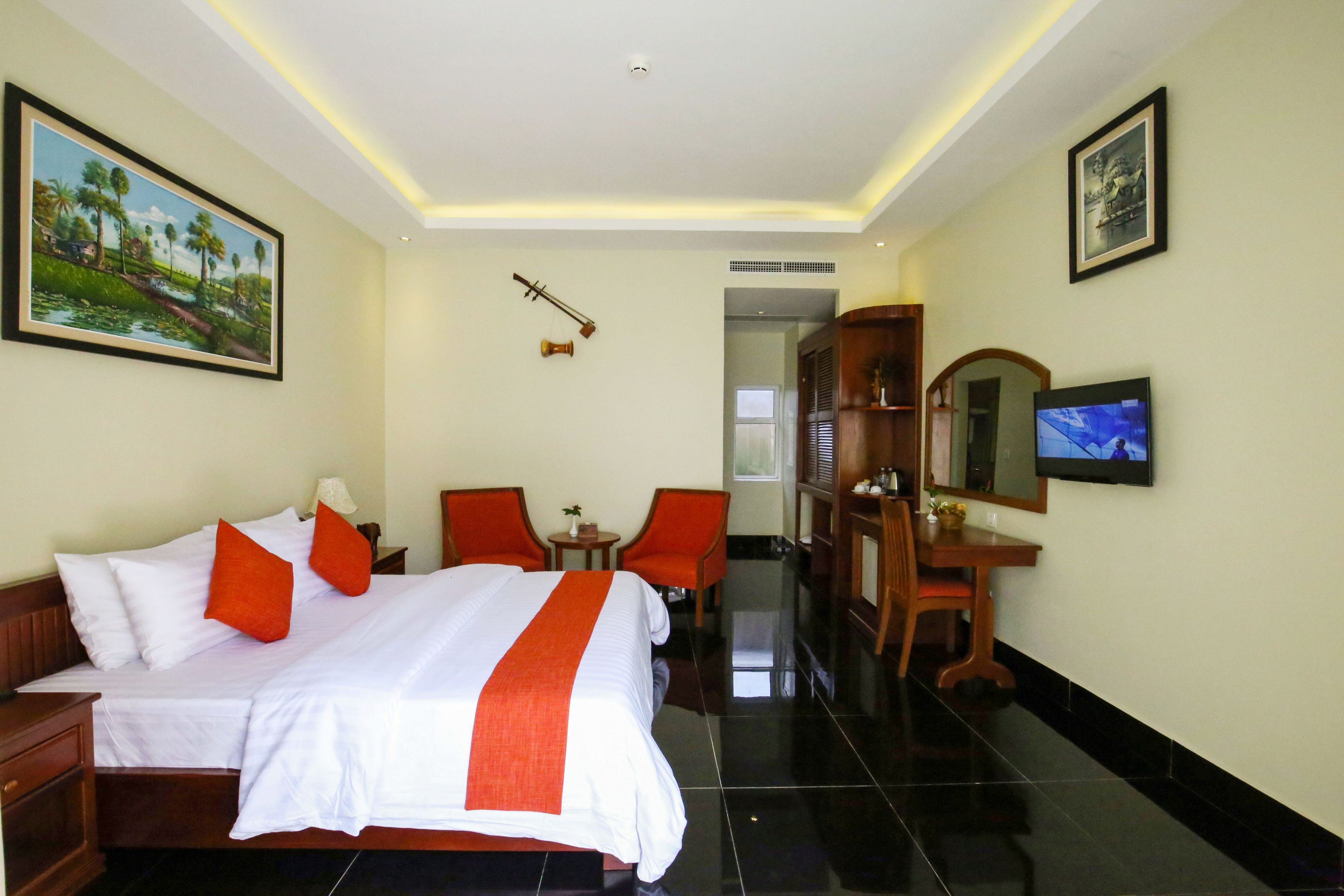 Una habitación de hotel con una cama grande, dos sillas, un escritorio con televisor y obras de arte en las paredes.