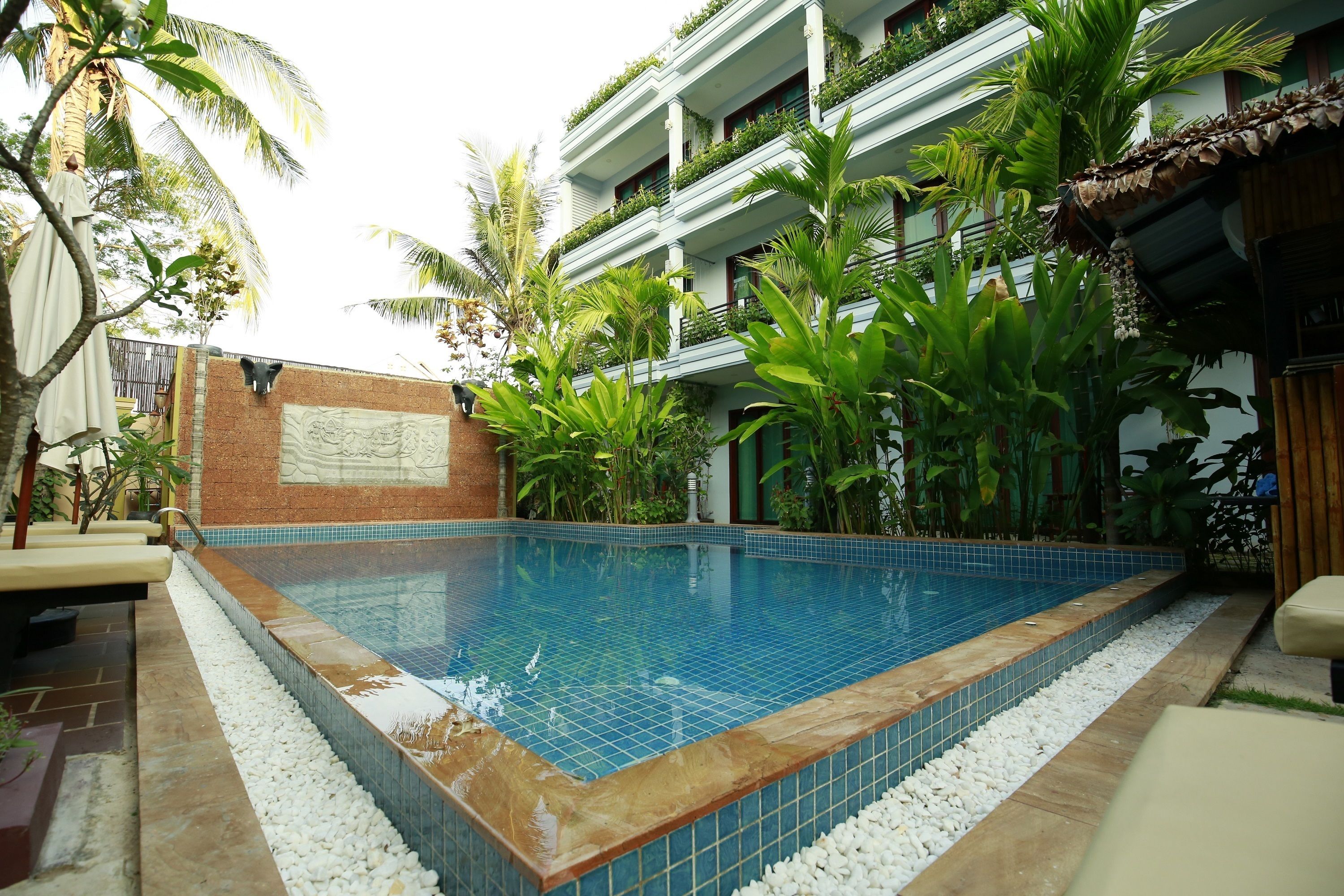 A rectangular swimming pool with blue tiles, surrounded by white pebbles, and bordered by a brick wall.