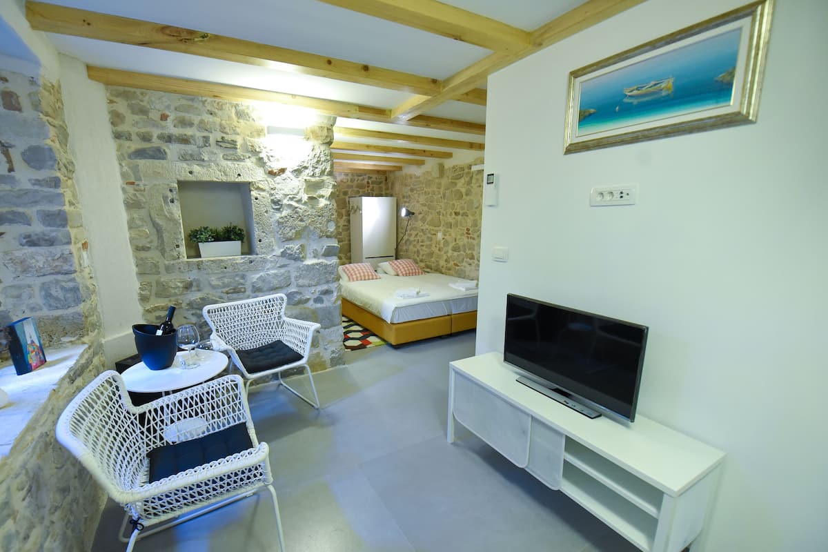 Ein gemütliches Zimmer mit Steinwand, einem Bett, einem Fernseher und Korbsesseln.