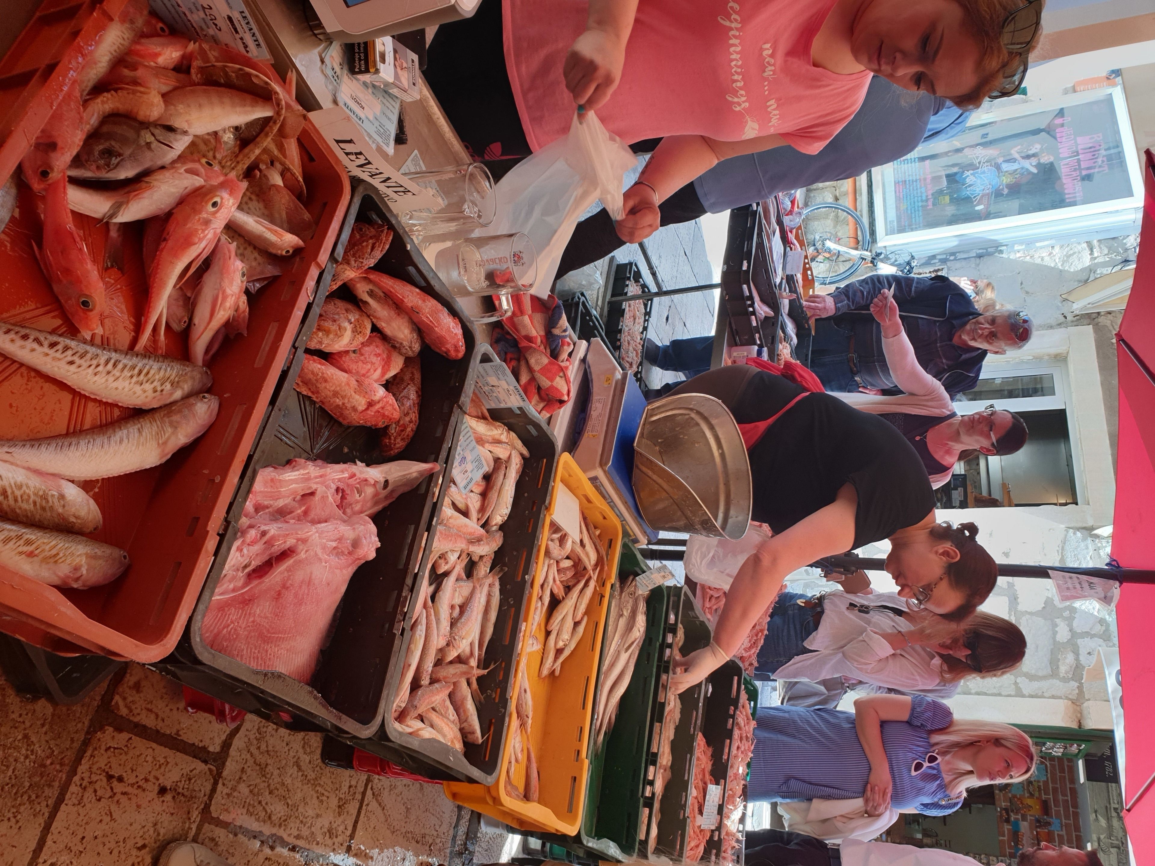 A market stall with various fresh fish displayed on trays and in bins.