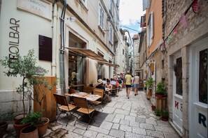 Una calle estrecha con mesas al aire libre en un restaurante, rodeada de edificios históricos.