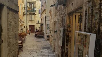 A narrow stone-paved alleyway between buildings with balconies and a shop on the right.