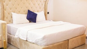 Un lit avec une tête de lit capitonnée, du linge de lit blanc et un oreiller bleu.