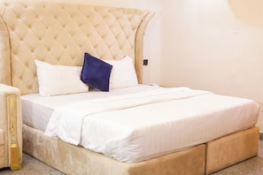 Un letto con testiera trapuntata, biancheria da letto bianca e cuscino blu.