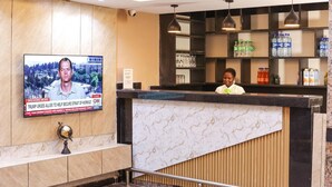 Un espace d’accueil d’hôtel avec un comptoir en marbre, un écran de télévision diffusant un bulletin d’information et des étagères remplies de bouteilles d’eau et de collations.