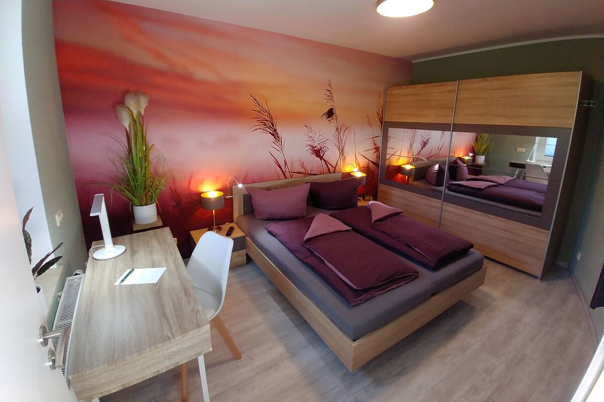 A modern bedroom with a bed, bedside tables, a desk, and a large mirror.