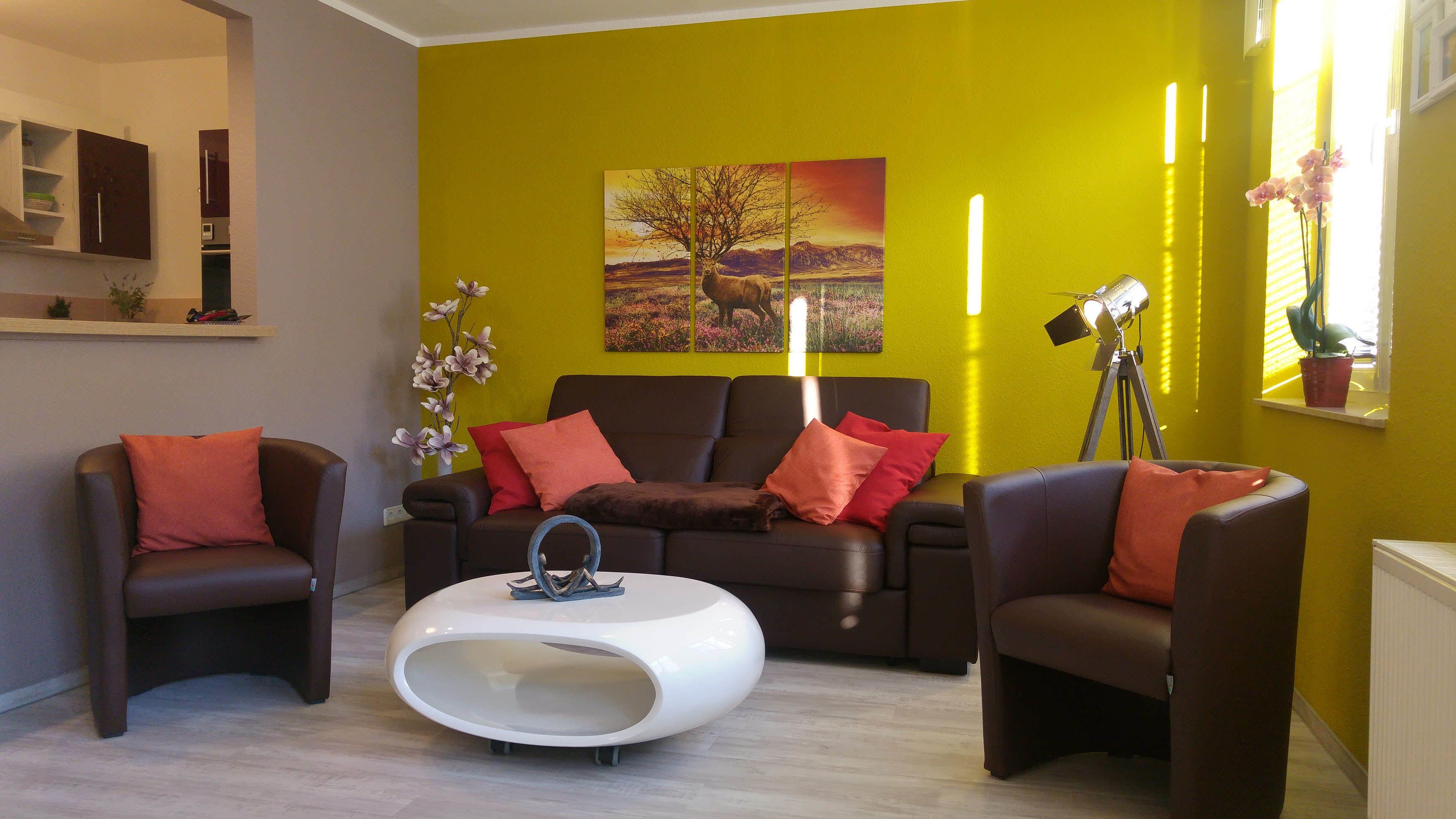 Un salon moderne avec un mur d’accent jaune, une grande peinture représentant un paysage et une table basse blanche.