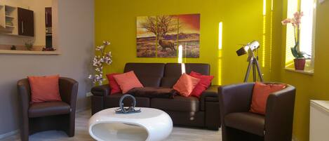 Un salon moderne avec un mur d’accent jaune, une grande peinture représentant un paysage et une table basse blanche.
