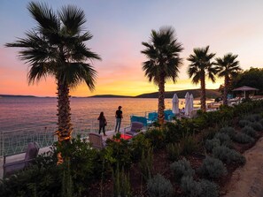 A coastal resort with palm trees, a pool area, and a view of the sea at sunset. - Mediteran Travel Mobile Homes Belvedere (Seget)