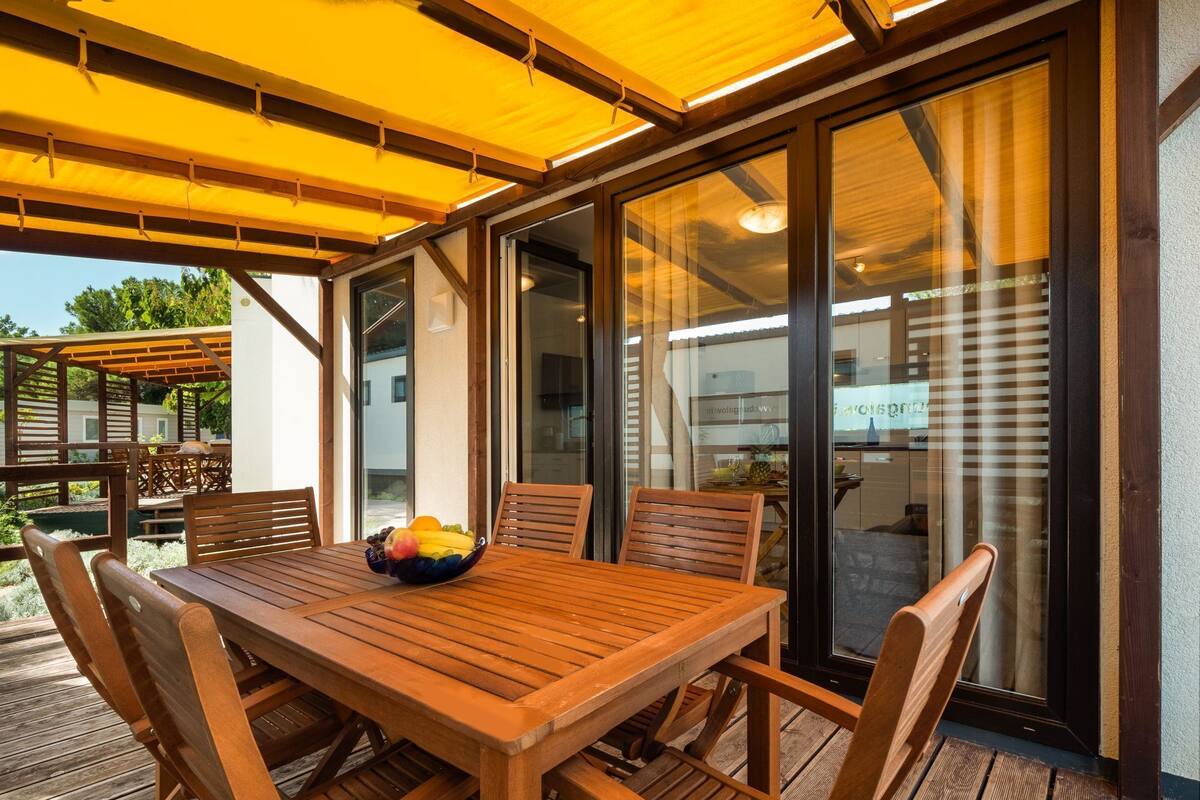 Eine Holzterrasse mit Tisch und Stühlen, einer Obstschale und einer Glastür, die zu einem Innenbereich führt.