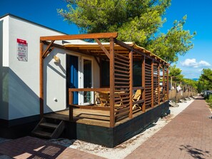 A row of wooden cabins with a covered patio area, a door, and a sign indicating a booking option. - Mediteran Travel Mobile Homes Belvedere (Seget)